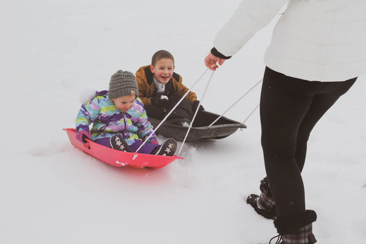 Two kids being pulled on sleds smiling